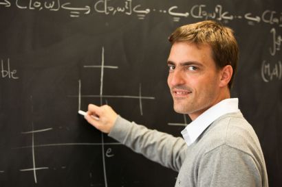 Un jeune homme tenant une craie devant un tableau avec des symboles mathématiques