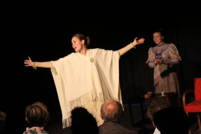 Deux étudiantes lettones sur scène, en costume d'époque, l'une ouvrant largement les bras.