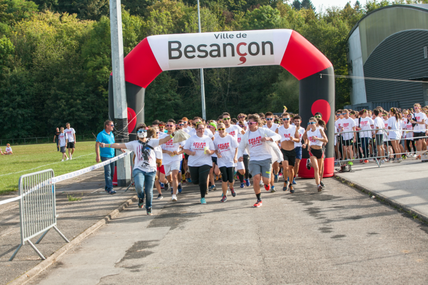Départ d'une course sous un portique estampillé "ville de besançon". Les étudiants qui courent portent tous le même tee shirt blanc