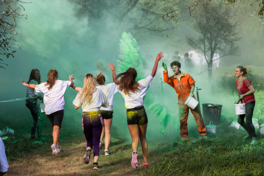 Des filles de dos qui courent et d'autres étudiants qui portent des seaux et qui leur jettent de la poudre verte.