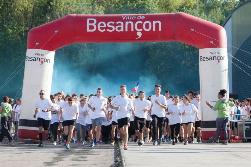 Une masse d'étudiants en tee-shirt blancs court. Derrière eux, un nuage de poudre bleue.