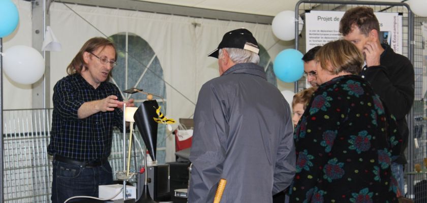 Un chercheur présentant un dispositif expérimental sur un stand avec des gens de dos.