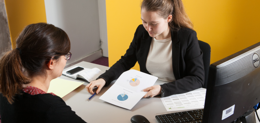 Deux jeunes femmes en tenue de travail en conversation à un bureau.