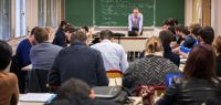 Une salle de classe avec de nombreux étudiants penchés sur leurs copies et au tableau Guy Labarre qui donne cours.