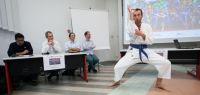 Un jeune homme en kimono dans une posture de karaté devant un jury de quatre personnes qui sourient.