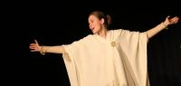 Deux étudiantes lettones sur scène, en costume d'époque, l'une ouvrant largement les bras.