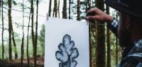 Kiven B affichant en forêt une de ses créations graphiques