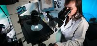 Une jeune femme en blouse regarde dans un microscope. On voit sur un écran les champignons qu'elle observe.