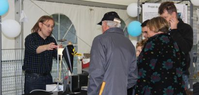 Un chercheur présentant un dispositif expérimental sur un stand avec des gens de dos.