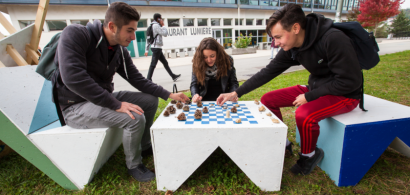 trois étudiants en train de jouer aux échecs sur du mobilier d'extérieur en carton.