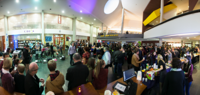 Vue panoramique de l'intérieur d'une bibliothèque pleine de monde, avec des gens debout et des musiciens.