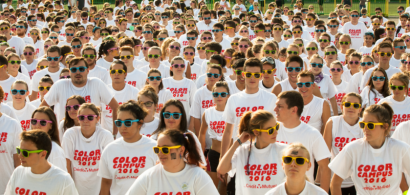 Un ensemble d'étudiants portant tous le même tee shirt blanc marqué "color campus 2016" et des lunettes de soleil colorées.