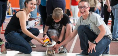 Trois collégiens rient accroupisd errirèe leur robot.