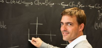 Un jeune homme tenant une craie devant un tableau avec des symboles mathématiques