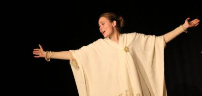 Deux étudiantes lettones sur scène, en costume d'époque, l'une ouvrant largement les bras.