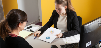 Deux jeunes femmes en tenue de travail en conversation à un bureau.
