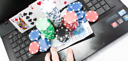 Des jetons de poker, cartes à jouer et billets posés sur un ordinateur portable