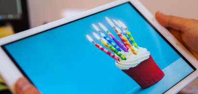 Des mains tiennent une tablette sur laquelle on voit un gateau d'anniversaire.
