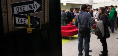 Un panneau avec une direction "one way" en premier plan un groupe de gens qui discutent en arrière-plan