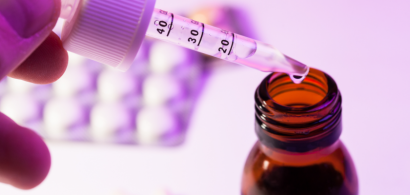 Gros plan sur un flacon de médicament et une pipette, avec en arrière plan une plaquette de médicaments.