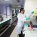 Nadia Crini en blouse dans le laboratoire manipule une pipette. On voit la salle en arrière-plan.