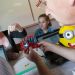 Une jeune fille explique queqlue chose à un adulte qui tient une partie du robot.