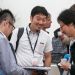 Trois jeunes hommes asiatiques discutent. L'uin regarde l'objectif en souriant.