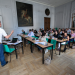 Grand salon de l'UFR SLHS : un homme parle devant de nombreux adultes.