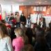 Salle d'exposition, plan large : un groupe d'étudiants fait visiter à des lycéens.