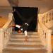 Un jeune homme en tenu de gala faisant des acrobaties sur une main dans un escalier