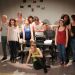 L'équipe du théâtre universitaire sur scène. Groupe de 12 personnes, hommes et femmes, debout devant une table où est posée une machine à écrire.