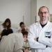 Portrait de Michael Boyer-Guittaut en blouse, un groupe d'étudiants en blouse derrière lui pendant un TP.
