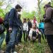 Un groupe d'étudiants dans la forêt autour de l'enseignante qui leur explique quelque chose, accroupie.