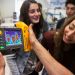 Deux jeunes filles regardent une caméra thermique où on voit des visages.