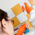 Une jeune femme de dos en blouse et gants oranges manipule une pipette.